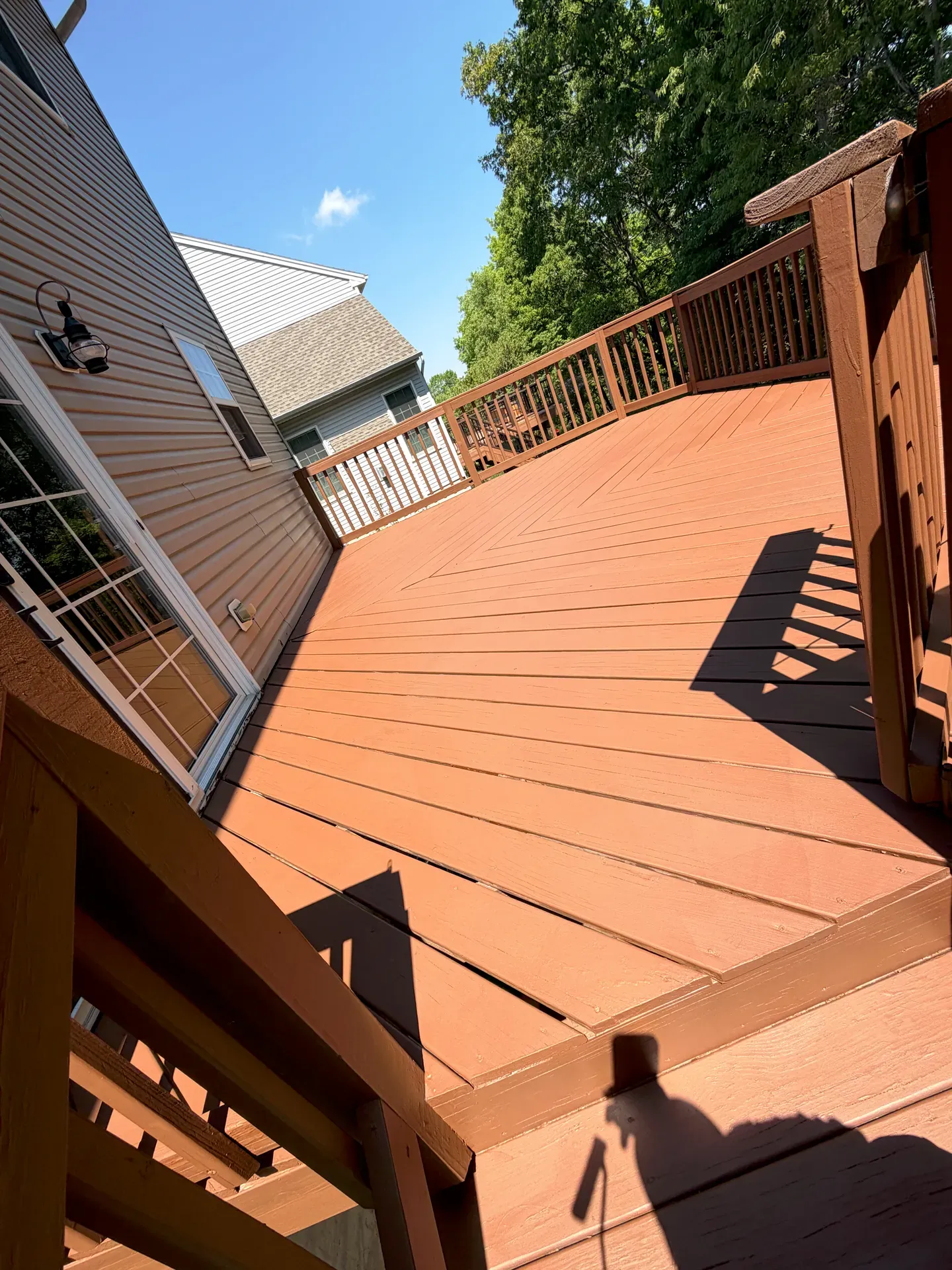 Backyard deck finished in a warm taupe-brown stain, ceiling fan and stair rail in matching tone, sunlit deck boards in late afternoon light