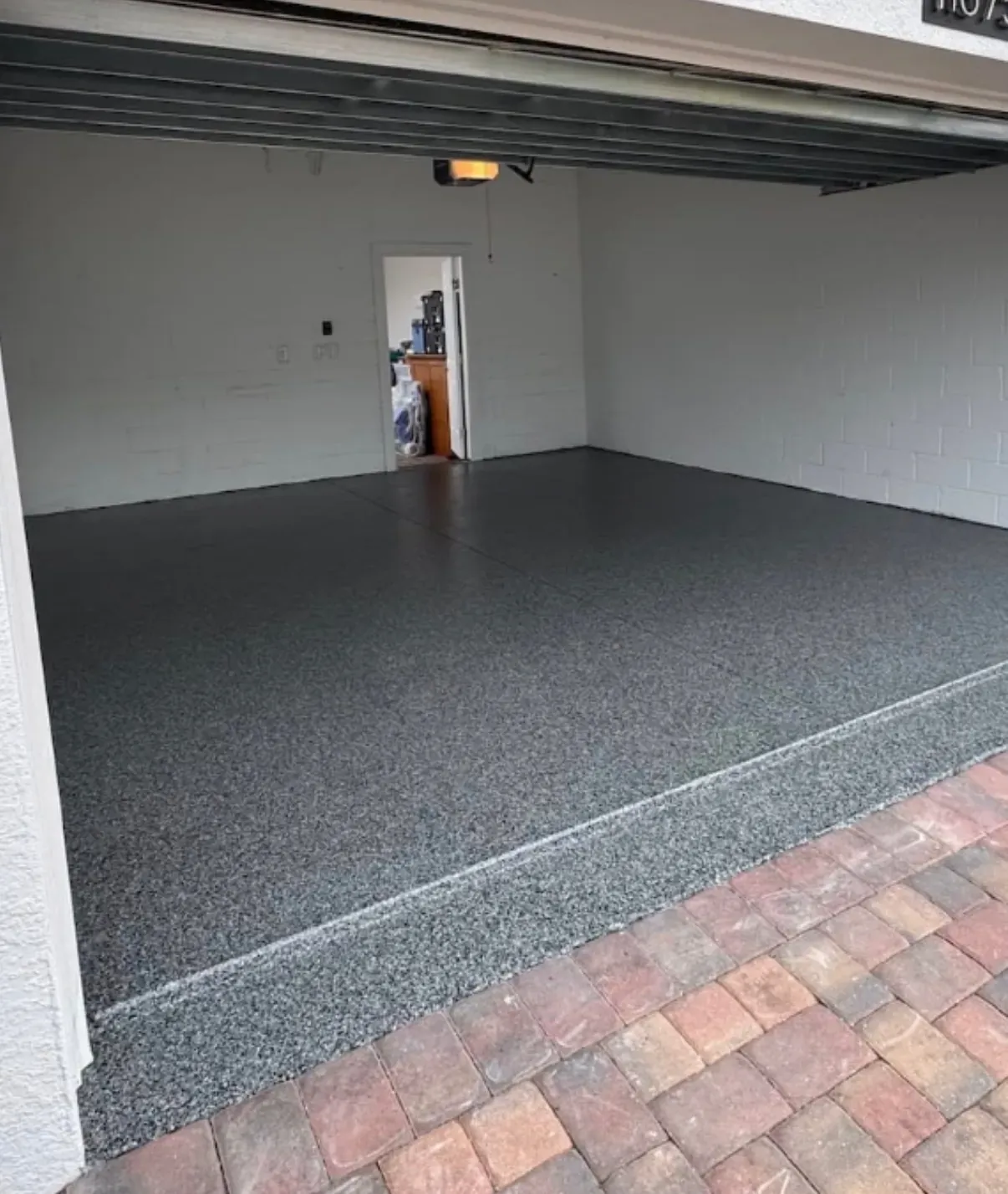 Two-car garage with gray epoxy and color-flake floor coating freshly applied, paver apron at the door threshold
