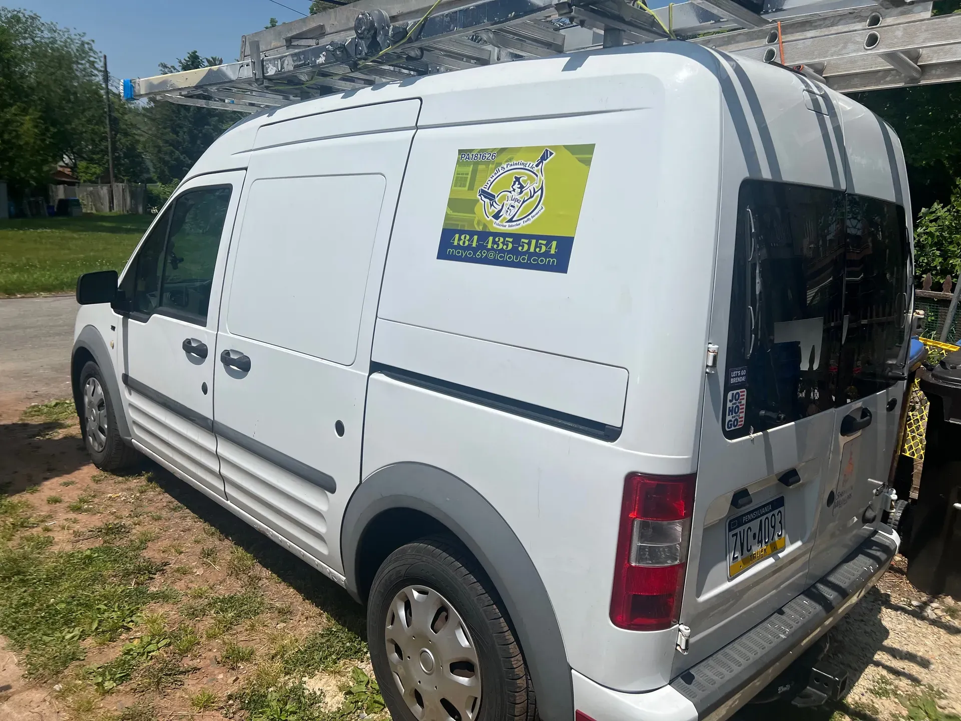 JL Drywall and Painting branded white work van with green-and-yellow decal at the workshop